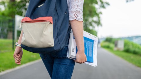 Ausschnitt einer Person von hinten mit Unterlagen im Arm