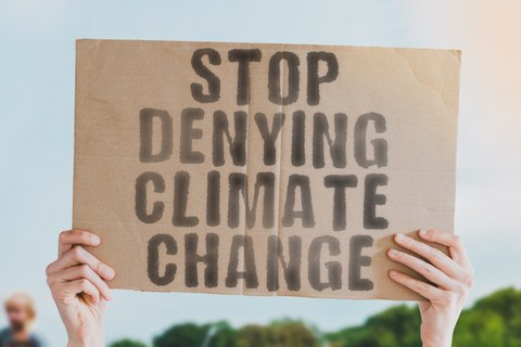 zwei Hände, die eine Pappschild hochhalten, auf welchem steh: Stop denying climate change