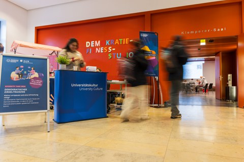 Der Eingang des Klemperersaals mit dem Empfangsbereich des Diversity Managements und dem Schriftzug "Demokratiefitnessstudio" an der Wand