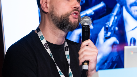 Foto von Christoph May, der in ein Mikrofon spricht.