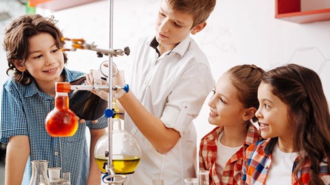 Vier Kinder stehen um ein chemisches Experiment mit Flüssigkeiten