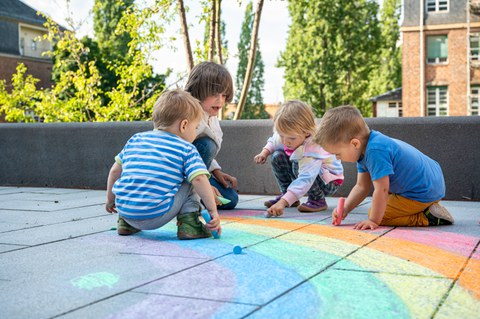 Foto von vier Kindern, die auf einem Steinweg auf dem TUD-Campus mit Kreide einen Regenbogen malen