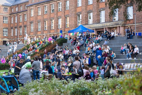 Four children draw with coloured chalk on the ground in the inner courtyard. A banner informs about the TUD Family Festival on 19 September from 3 pm in the inner courtyard of the FOE. The children are engrossed in their creative endeavours, surrounded by