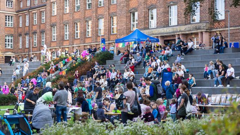 Four children draw with coloured chalk on the ground in the inner courtyard. A banner informs about the TUD Family Festival on 19 September from 3 pm in the inner courtyard of the FOE. The children are engrossed in their creative endeavours, surrounded by