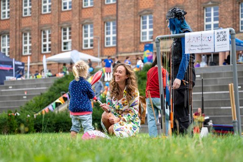 Das Foto zeigt eine Frau im geblümten Kleid, die mit Ihren Tochter beim Familienfest mit Keulen jongliert.