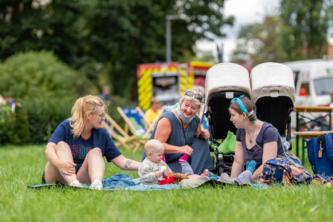 Drei Frauen unterschiedlichen Alters und zwei kleine Kinder sitzen beim Familienfest auf der Wiese auf einer Picknickdecke.
