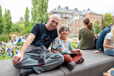 Das Foto zeigt einen Mann und ein Kind, die in die Kamera lächeln.
