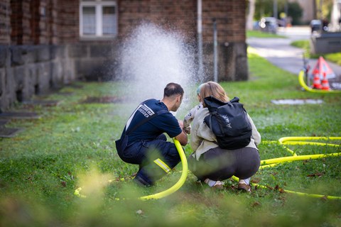 Feuerwehrmann, Elternteil plus Kind beim Spritzen mit Schlauch