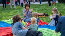 Wiese mit bunter Plane, auf der Kinder sitzen und musizieren