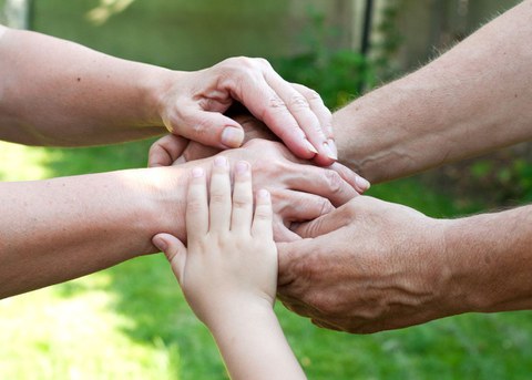 Auf dem Foto sieht man die Hände mehrerer Personen unterschiedlichen Alters, die übereinander liegen und sich gegenseitig halten.