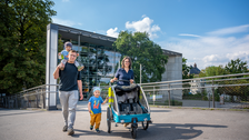 Foto zeigt Eltern mit zwei Kleinkindern und einem Kinderwagen auf dem Campus der TU Dresden.