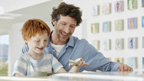 Foto zeigt, wie Vater und Sohn zusammen an einem Tisch mit Holzfiguren spielen.