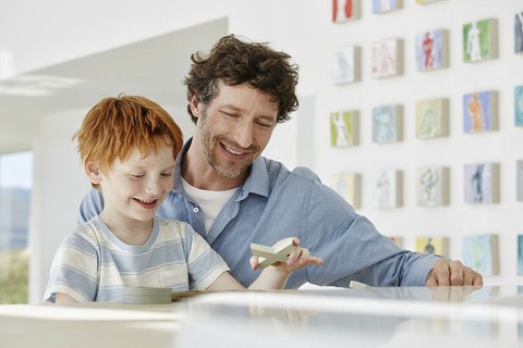 Foto zeigt, wie Vater und Sohn zusammen an einem Tisch mit Holzfiguren spielen.