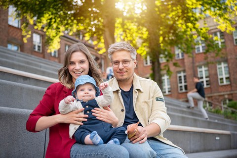 Mutter, Vater, Kind sitzen auf der Steintreppe hinter dem Fritz-Foerster-Bau.