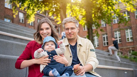 Mother, father and child are sitting on the stone steps behind a red brick building.