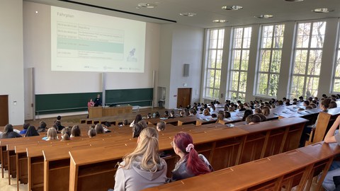 Impression von der Eröffnung des Girls' & Boys' Day 2026 in einem Hörsaal. Schüler:innen verfolgen einen Vortrag mit Powerpoint-Präsentation.