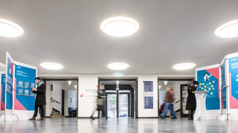 Menschen bewegen sich durch das Foyer, einige lesen die Ausstellungstafeln.