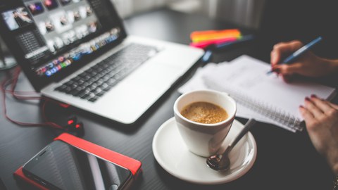 Foto von einem Arbeitsplatz mit Laptop, Kopfhörern, Handy Timer und einem Kaffee.