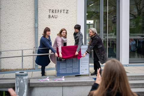 Vier Frauen heben einen rotes Tuch zur Eröffnung einer Schautafel