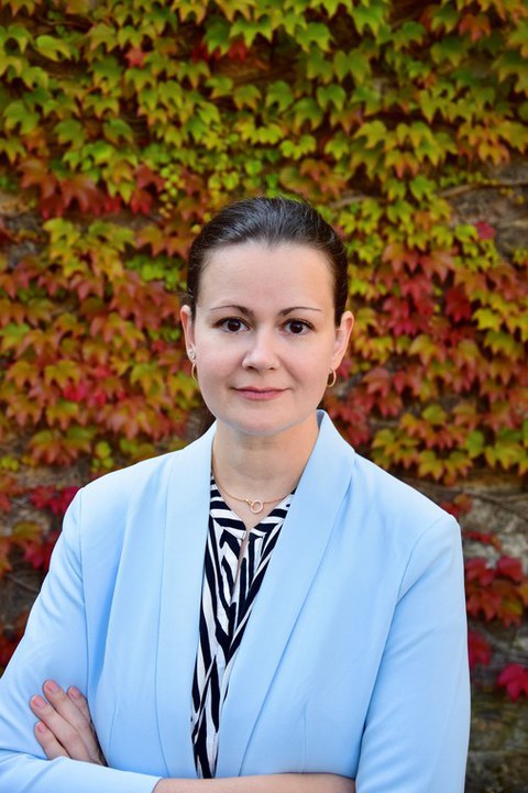 Frau mit blauem Blazer und verschränkten Armen schaut in die Kamera.