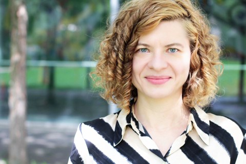 Frau mit kurzen lockigen Haaren schaut lächelnd in die Kamera.