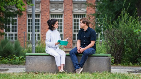 A man and a woman sit on a bench at the lecture theatre centre and study together