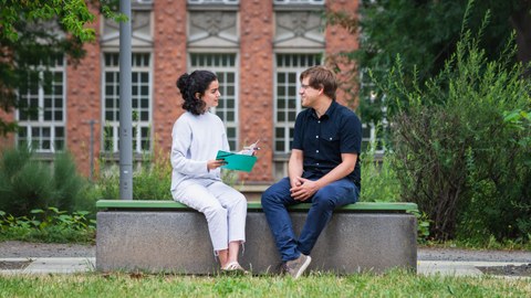 Ein Mann und eine Frau sitzen auf einer Bank am Hörsaalzentrum und lernen zusammen