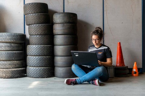 Woman sits cross-legged on the floor next to three columns of tyres with a laptop in her hands