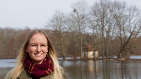 Das Foto zeigt Henriette Heinrich vor einem Teich. Im Hintergrund ist ein kleines Häuschen auf einer kleinen Insel zu sehen.