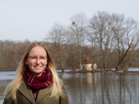 Das Foto zeigt Henriette Heinrich vor einem Teich. Im Hintergrund ist ein kleines Häuschen auf einer kleinen Insel zu sehen.