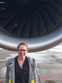 Das Bild zeigt eine Frau vor einem riesigen Flugzeugtriebwerk.