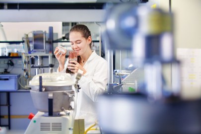 Das foto zeigt eine junge Frau im Labor, die ein Gefäß geöffnet hat und daran riecht. 