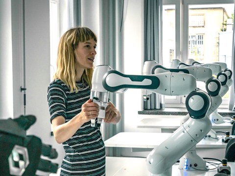 Auf dem Bild ist eine Frau zu sehen die einen Roboterarm bedient. Im Hintergrund sind weitere Roboterarme zu sehen.