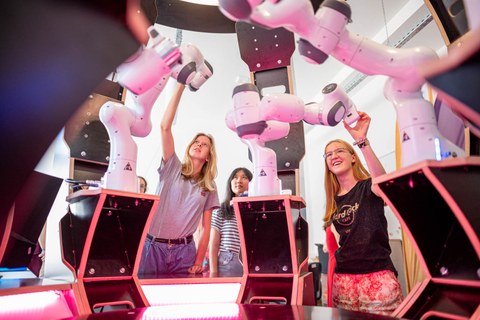 Drei junge Frauen bedienen Roboterarme.