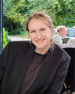 Portraitfoto einer Frau mit blonden Haare und schwarzem Sakko vor grünem Hintergrund