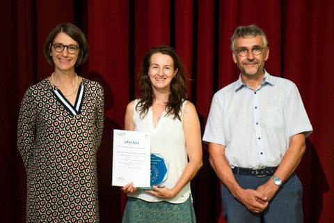 Three people are standing together and one person is holding an award.