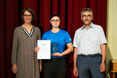 Three people are standing together and one person is holding an award.