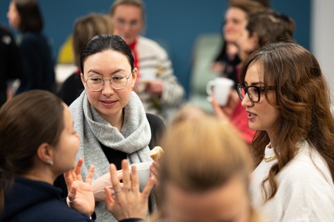 Eine Gruppe von Frauen unterhält sich, mit Essen und Getränken in den Händen, beim Women@DDc Neujahrsempfang. Im hintergrund sind weitere Frauengruppen zu sehen.