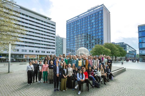  Large group gathered outdoors in front of modern buildings for a group photo, many people standing together.