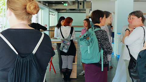 Menschen stehen in hellem Innenraum in kleinen Gruppen zusammen und unterhalten sich während einer Pause.