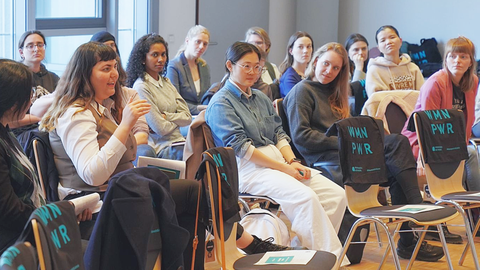 Seminarraum mit Publikum, eine Person spricht und gestikuliert, andere hören aufmerksam zu.