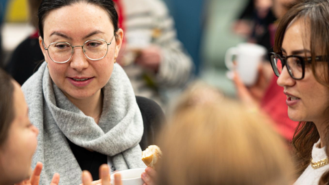 Nahaufnahme einer Gesprächsrunde, mehrere Personen reden und halten Tassen in den Händen, lebhafter Austausch.