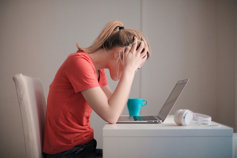 Frau sitz an einem Schreibtisch und lässt den Kopf hängen. Vor ihr steht ein Laptop.