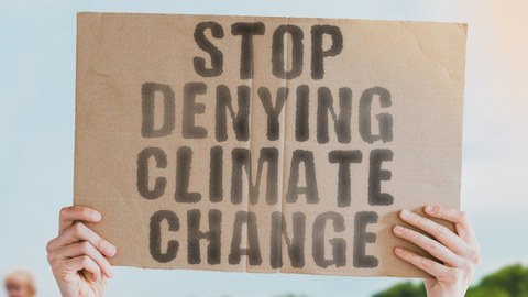 2 hands hold sign in the air that says "Stop denying climate change".