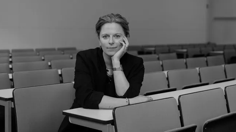 Schwarz-Weiß-Porträt. Lisa Niendorf sitzt im Hörsaal. Sie stützt ihre Hand auf.