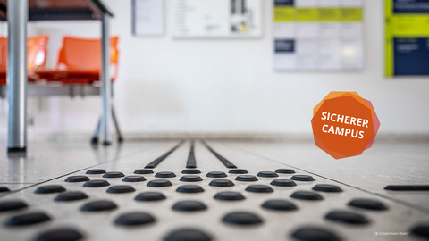 The photo shows black floor indicators that lead to information signs on the wall and serve as orientation aids for blind people.