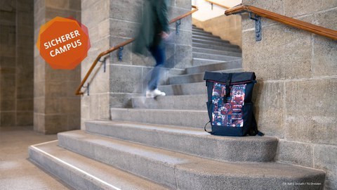 A backpack leans against a staircase. In the background one sees a lower body climbing the stairs.