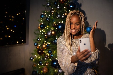 Frau sitzt vor einem Weihnachtsbaum und schaut  lächelnd in ihr Handy