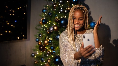 Frau sitzt vor einem Weihnachtsbaum und schaut  lächelnd in ihr Handy