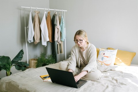 Frau sitz auf dem Bett und betreibt Homeoffice